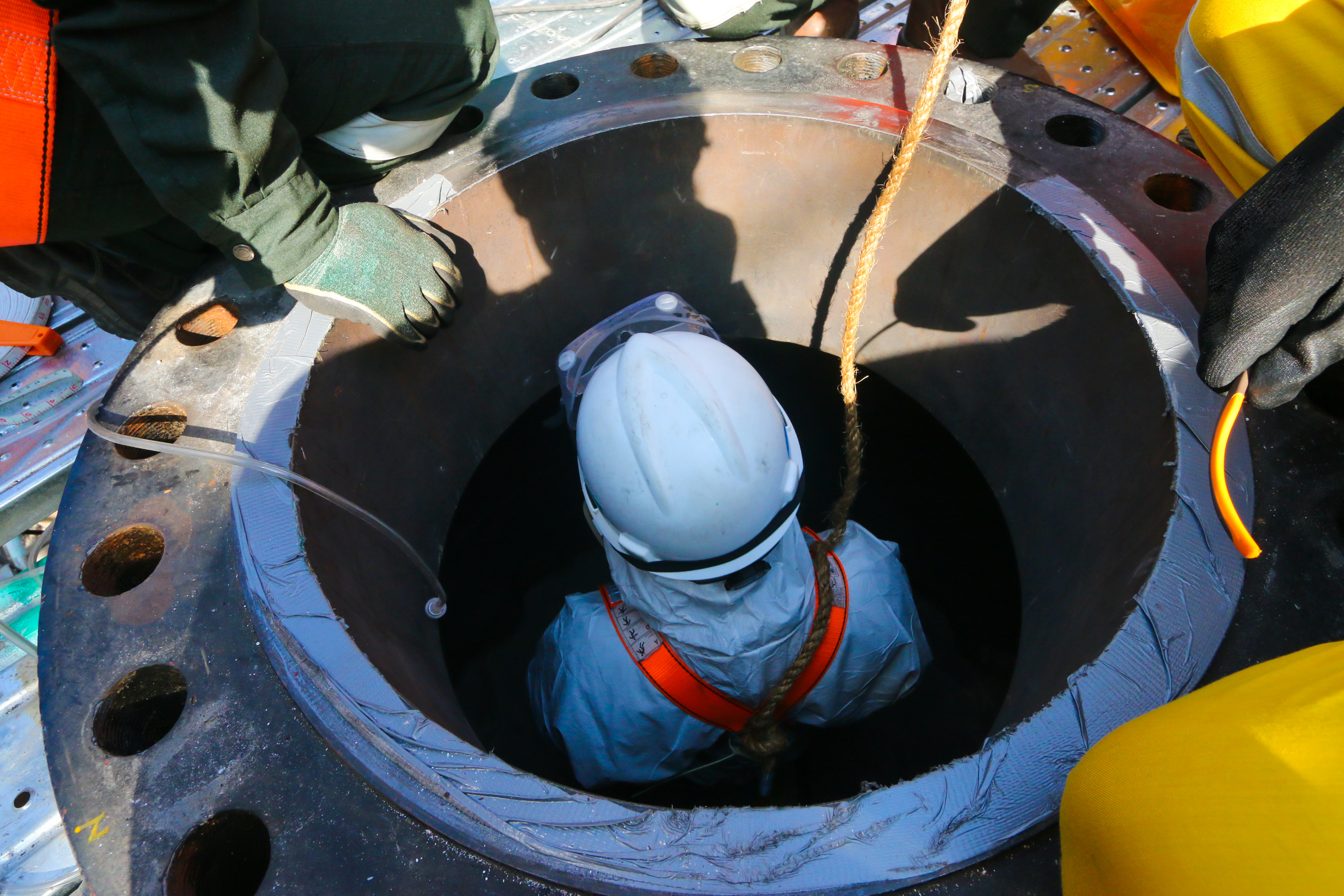 Confined space entry by a worker who wear white chemical suit.
